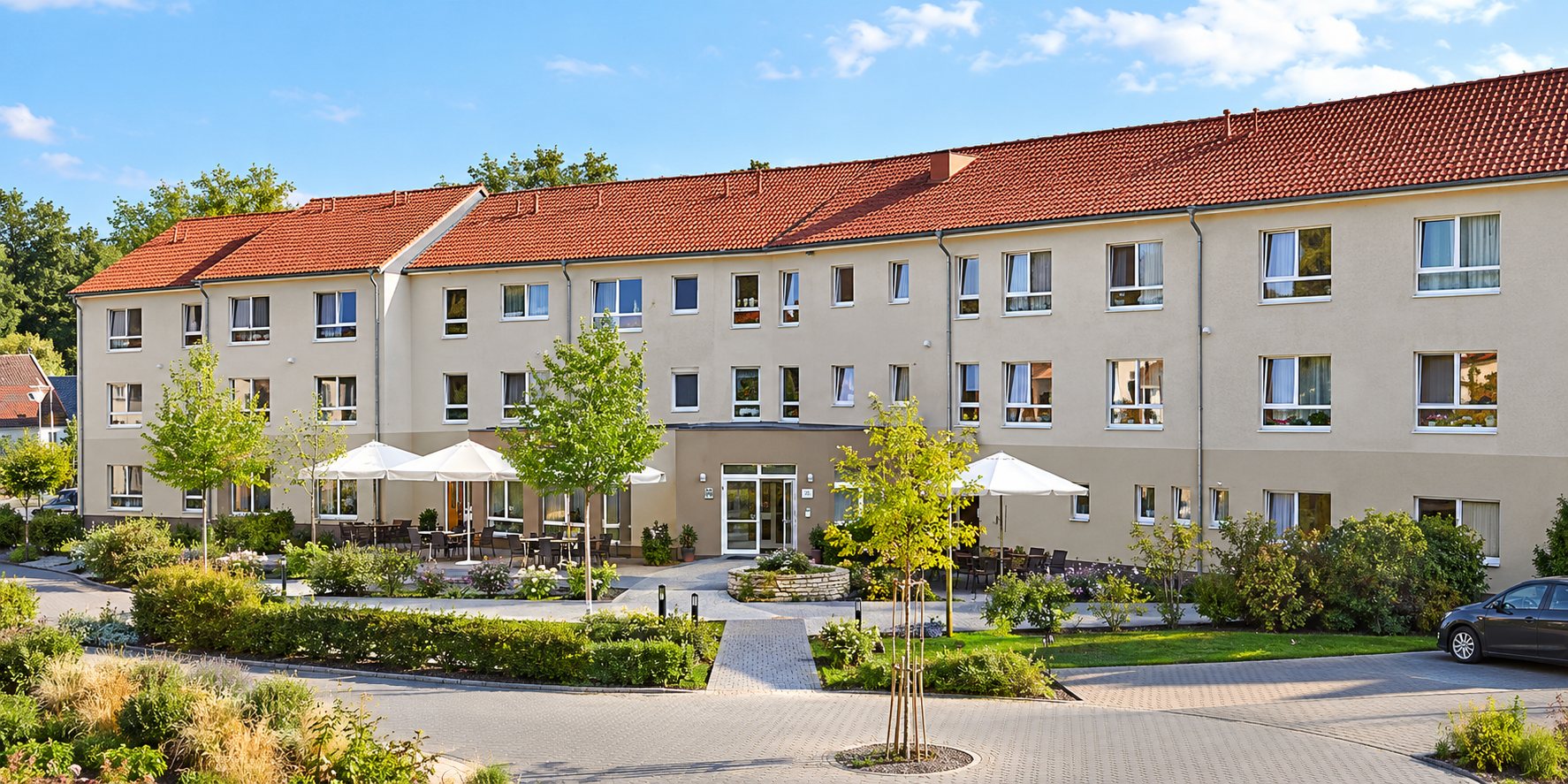 Pflegeheim mit Garten, Sonnenschirmen und rotem Ziegeldach